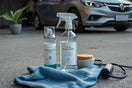 Eco-friendly car cleaning items and reusable cloth arranged beside a modern car exterior in daylight
