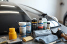 Car detailing products and microfiber towels arranged on a workbench near a glossy car hood