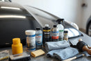 Car detailing products and microfiber towels arranged on a workbench near a glossy car hood