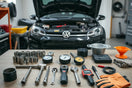 Organized car maintenance tools on a garage workbench with an open car hood in the background