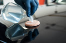 Gloved hand applying clear car coating agent to glossy dark paint for a fast, reflective finish