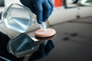 Gloved hand applying clear car coating agent to glossy dark paint for a fast, reflective finish