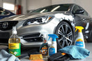 Car care products on a clean workbench beside a partially washed sedan