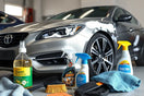 Car care products on a clean workbench beside a partially washed sedan