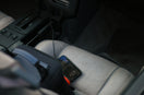 A smartphone charging on a grey car seat next to a black bag