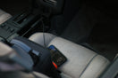 A smartphone charging on a grey car seat next to a black bag